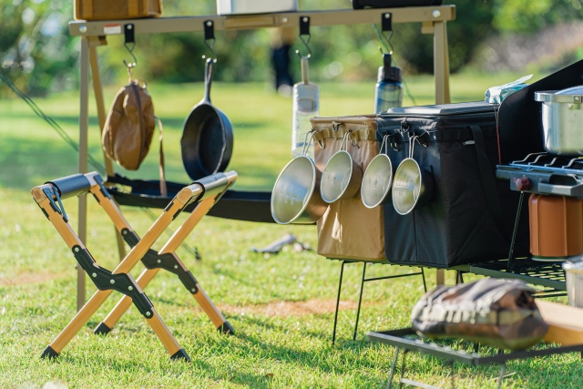 芝生のキャンプサイトの上で並べられたシェラカップなどの調理器具